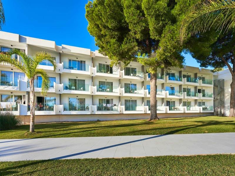Modern multi-story hotel surrounded by palm trees and lawns under a clear sky.