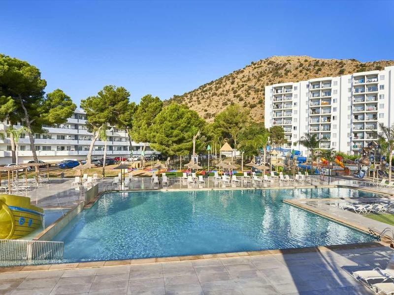 Large outdoor pool with surrounding lounge chairs and multi-story hotel building in the background.