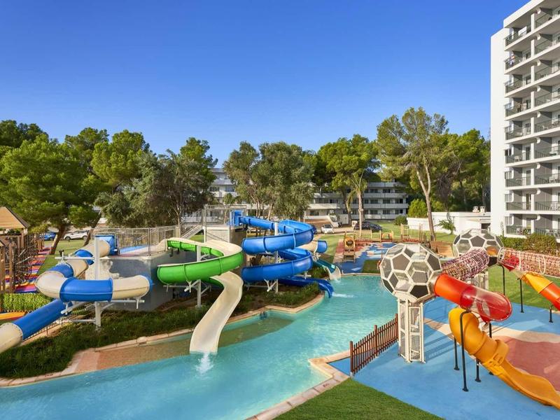 Water park with colorful slides and playground next to a white multi-story hotel building.