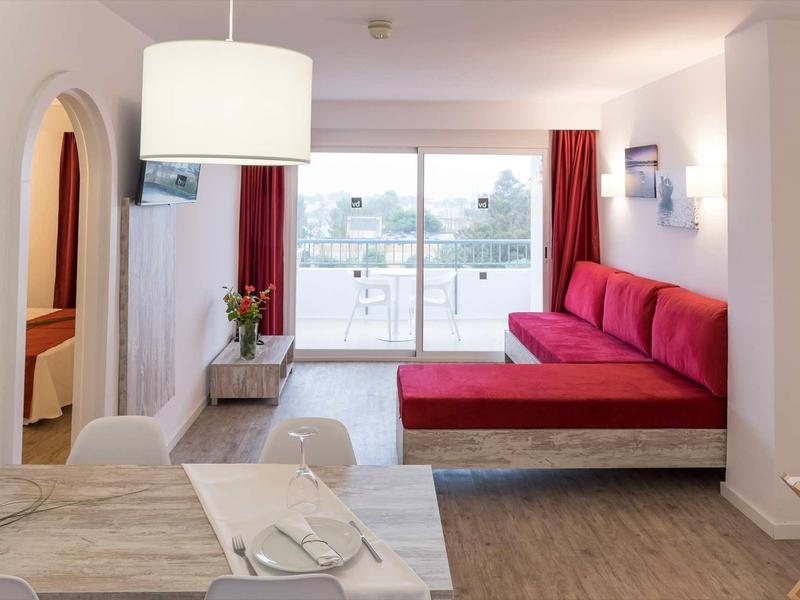 Modern hotel room with red sofa, balcony, and dining table.
