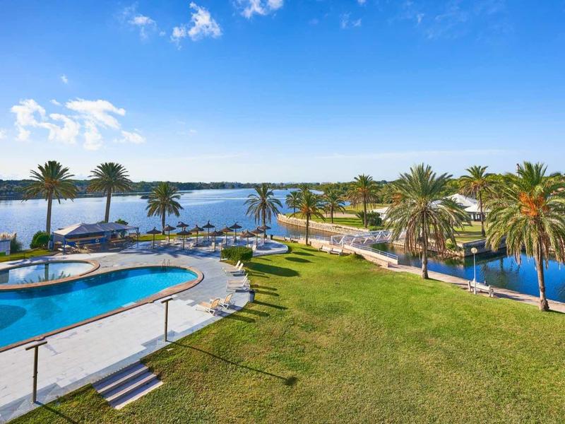 Spacious hotel area with pool, palm trees, and calm sea bay view under clear sky.