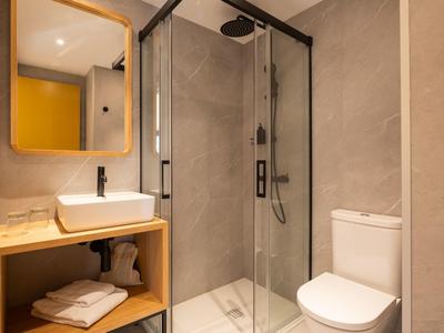 Salle de bain moderne avec douche en verre, WC blanc et lavabo sur étagère en bois.