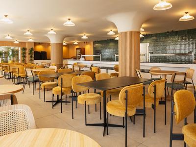 Salle de petit-déjeuner moderne et spacieuse avec des chaises jaunes et des tables en bois dans un hôtel.