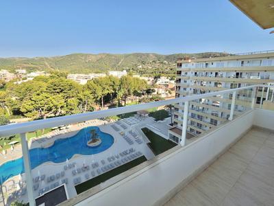 Balcony with railing overlooking pool and green hills under clear sky.
