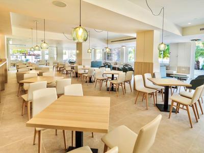 Bright, modern restaurant with wooden chairs and tables, large windows, and decorative hanging lamps.