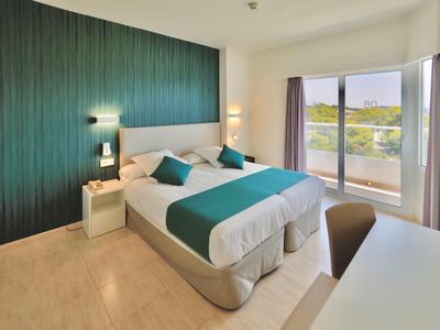 Modern hotel room with two beds, green accent wall, and balcony overlooking nature.