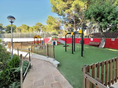 Children's playground with slide, swings, and climbing frame on artificial grass beside a walkway