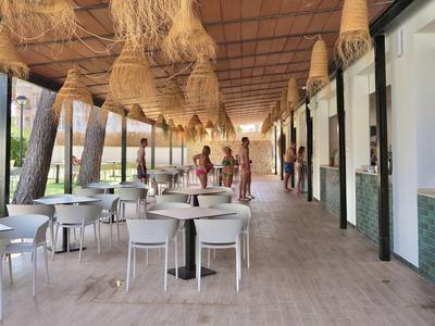 Covered outdoor area of a hotel with tables, chairs, and woven lamps.