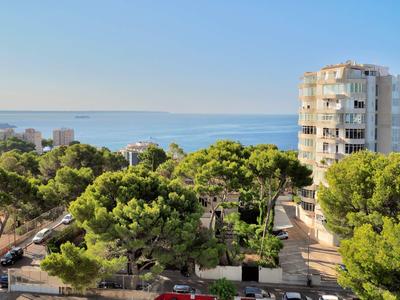 View of green trees and buildings with the sea in the background under clear sky.