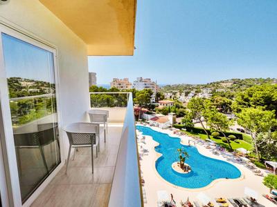 Balcony with chair and table overlooking pool and lush hotel garden area.