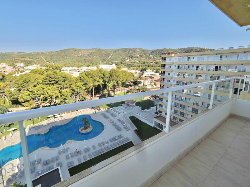 Balcony with railing overlooking pool and green hills under clear sky.