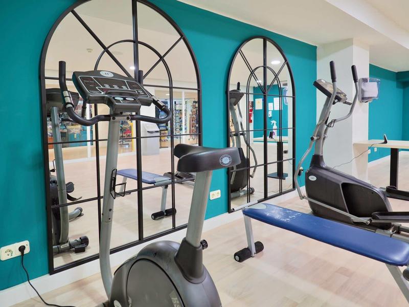 Modern gym with exercise equipment in front of a wall with decorative mirrors.
