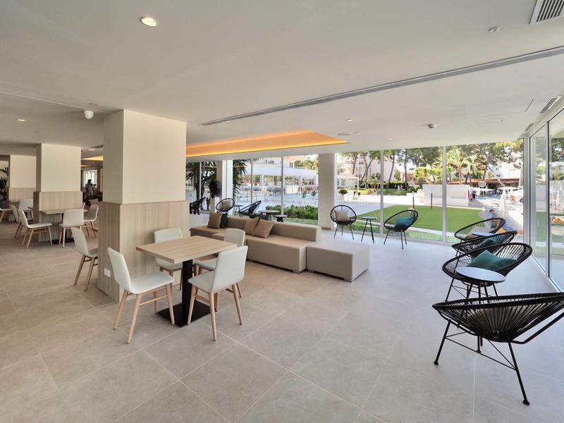 Modern hotel lobby area with seating groups and large glass windows overlooking garden.