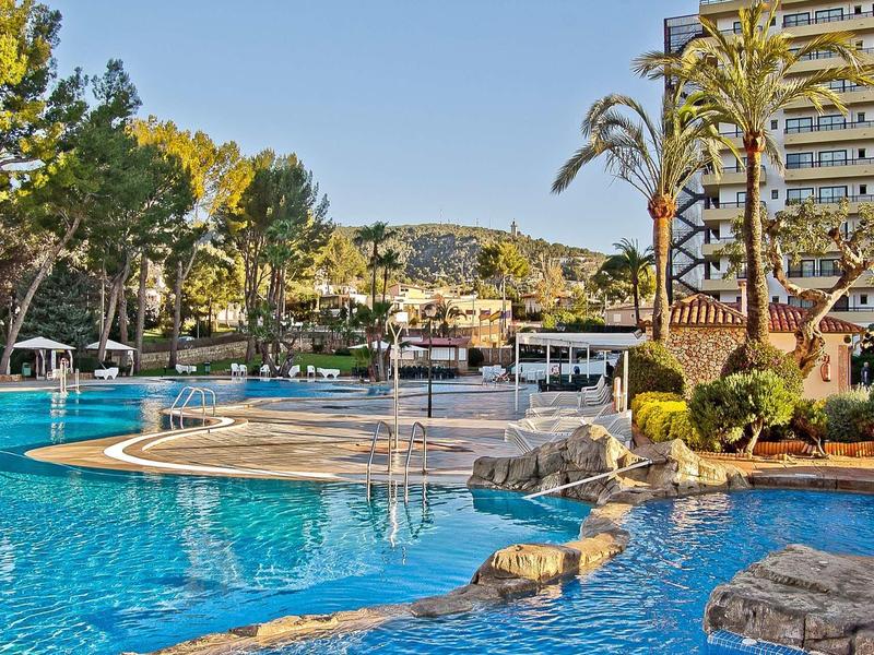 Large swimming pool with palm trees and hotel building in sunny weather.
