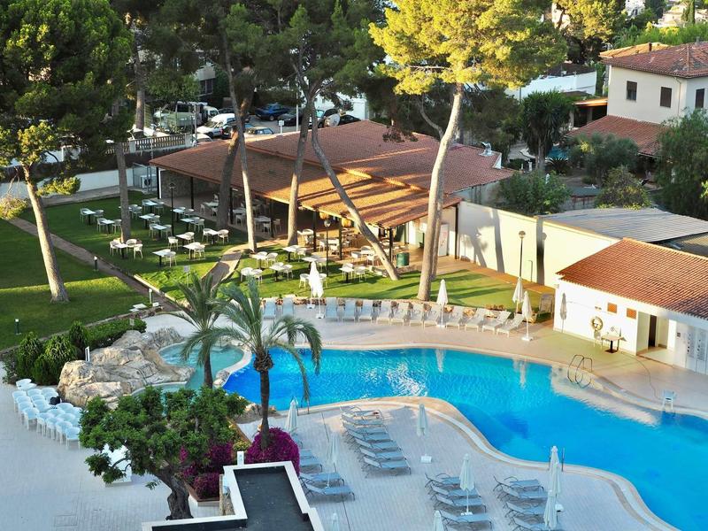 Hotel pool area with sun loungers and surrounding green garden landscape.
