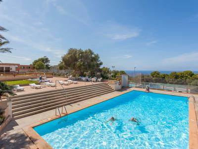 Piscine extérieure avec eau bleue et chaises longues, vue sur la mer et ciel partiellement nuageux