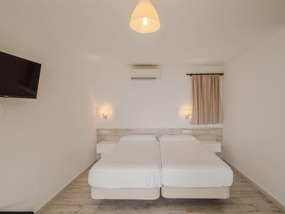 Chambre d'hôtel simplement meublée avec deux lits simples et une télévision moderne fixée au mur.