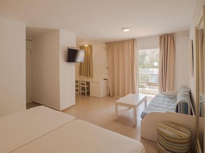 Chambre d'hôtel lumineuse avec deux lits, canapé, télévision et balcon avec rideaux.