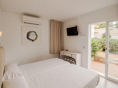 Chambre d'hôtel lumineuse avec lit double, télévision murale et porte-fenêtre donnant sur le jardin.