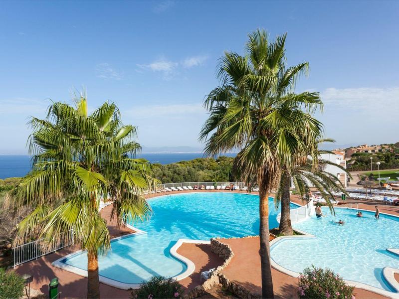 Zone piscine avec parasols et palmiers offrant une vue sur la mer sous un ciel clair.