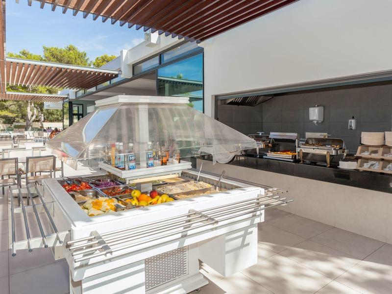 Buffet extérieur lumineux d'hôtel avec fruits frais et plats sous une pergola.