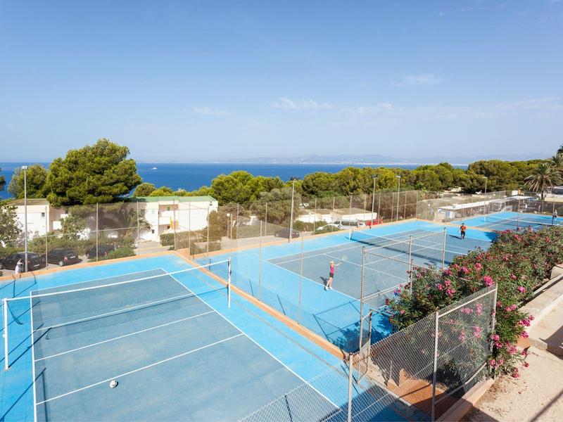 Vue de plusieurs terrains de tennis avec la mer en arrière-plan sous un ciel bleu.