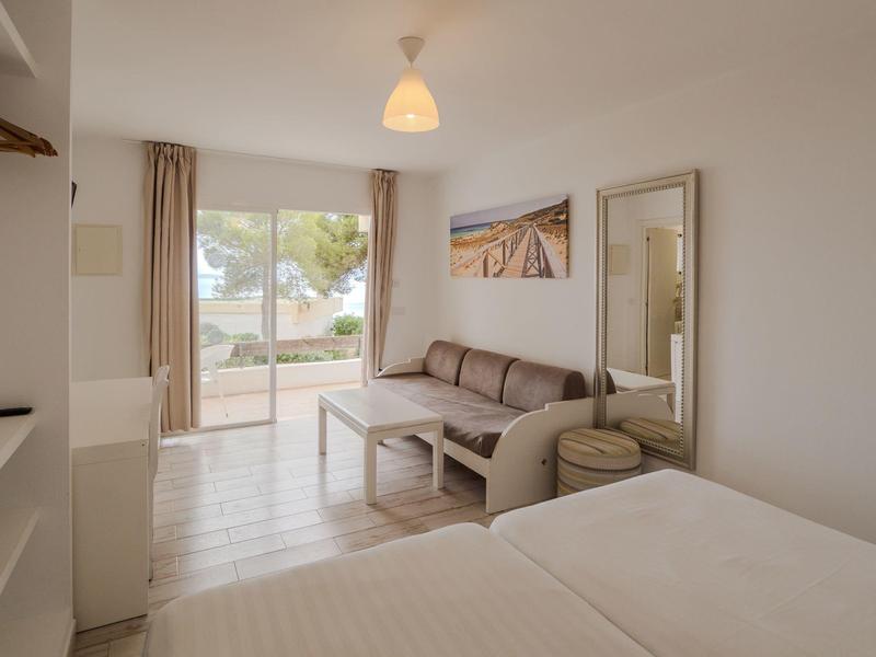 Chambre d'hôtel lumineuse avec lit, canapé, table et grande fenêtre donnant sur l'extérieur.