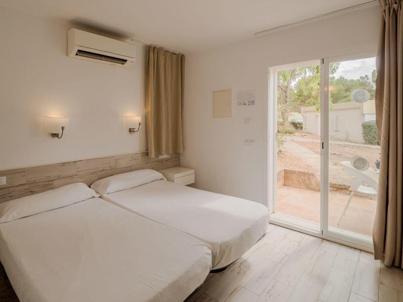 Chambre d'hôtel avec deux lits simples, climatisation et porte-fenêtre avec vue extérieure.