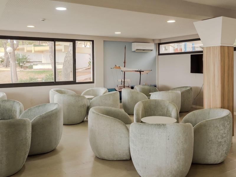 Un lounge d'hôtel lumineux avec des fauteuils ronds gris, de grandes fenêtres et une télévision murale.