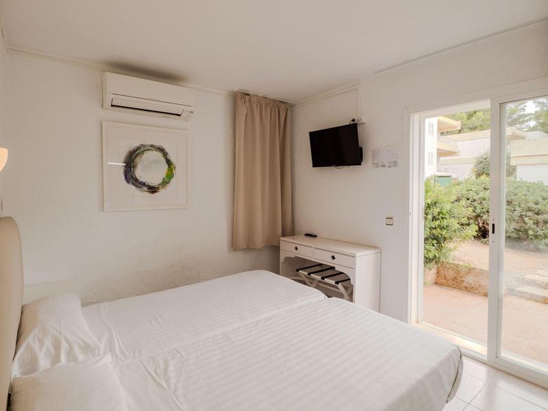 Chambre d'hôtel lumineuse avec lit double, télévision murale et porte-fenêtre donnant sur le jardin.