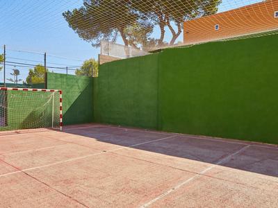 Leerer kleiner Sportplatz mit rotem Boden, grünem Zaun und Tor im Freien unter blauem Himmel.