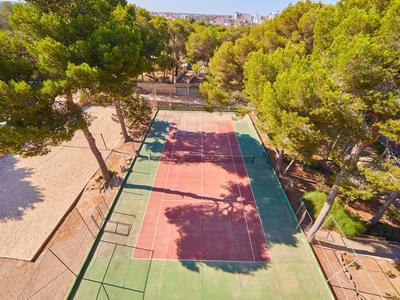 Leerer Tennisplatz mit grün-rotem Belag, umgeben von Bäumen und Sonnenschein.