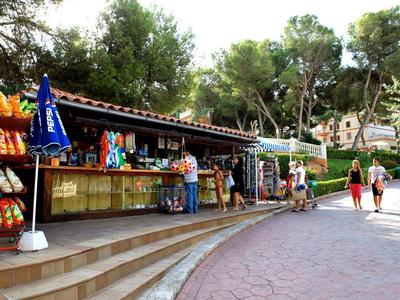 Ein Kiosk mit bunten Snacks und Getränken, umgeben von Bäumen und einem gepflasterten Weg.
