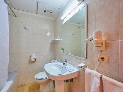 Kleine, helle Badezimmer mit Waschbecken, Toilette, Duschvorhang und großen Wandfliesen.