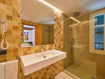Modernes Badezimmer mit beige gefliesten Wänden, großem Spiegel, Waschbecken und begehbarer Dusche.