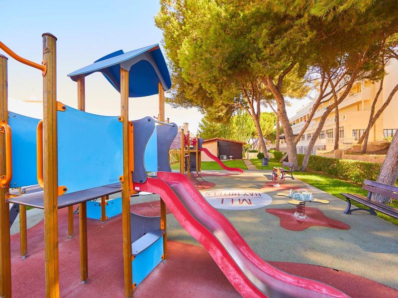 Kolorowy plac zabaw z zjeżdżalnią w zalesionym ogrodzie hotelowym.