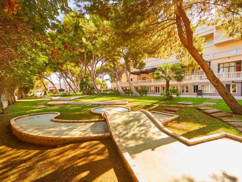 Słoneczny ogród hotelowy z drzewami i krętymi ścieżkami, spokojna i zielona atmosfera.