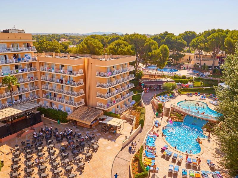 Widok z góry na hotel z basenem i słonecznymi miejscami do wypoczynku w otoczeniu drzew.