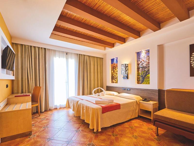 Jasny pokój hotelowy z podwójnym łóżkiem, drewnianym wystrojem i sofą.