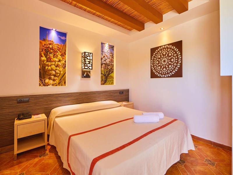 Prosty pokój hotelowy z podwójnym łóżkiem, jasnymi ścianami i kolorowymi dekoracjami.