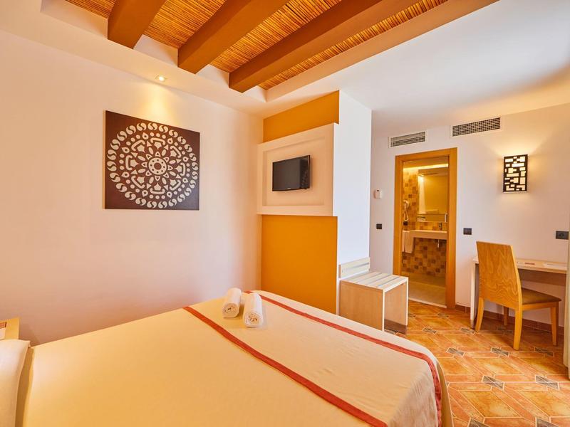 Jasny pokój hotelowy z drewnianymi belkami, podwójnym łóżkiem, biurkiem i dekoracją ścienną.