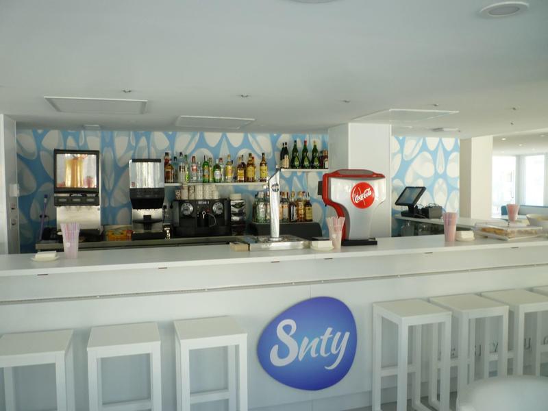 Area bar moderna con sgabelli bianchi e distributore di bevande in uno spazio luminoso.