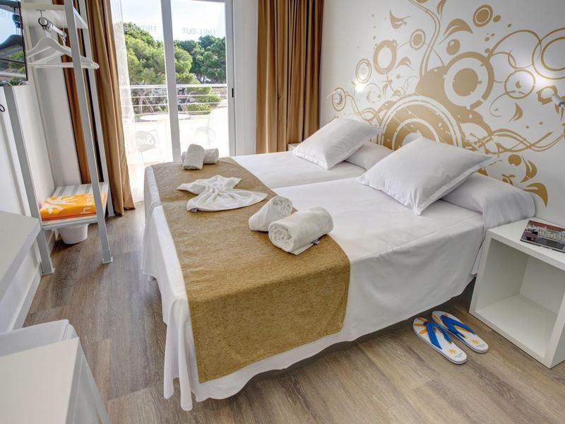 Una camera d'hotel moderna con letto matrimoniale, copriletto dorato e asciugamani bianchi.