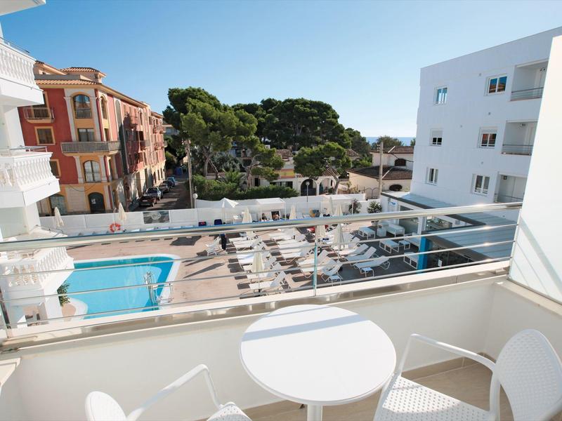Vista dal balcone con tavolo bianco sulla piscina dell'hotel e lettini sotto un cielo sereno.