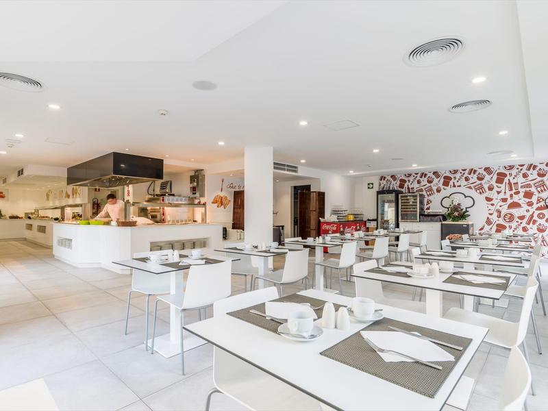 Sala colazioni luminosa con tavoli bianchi, sedie e area buffet.