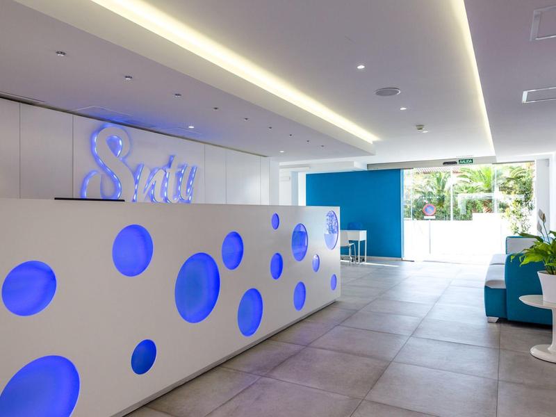 Reception moderna dell'hotel con bancone bianco e accenti blu in uno spazio luminoso e aperto.