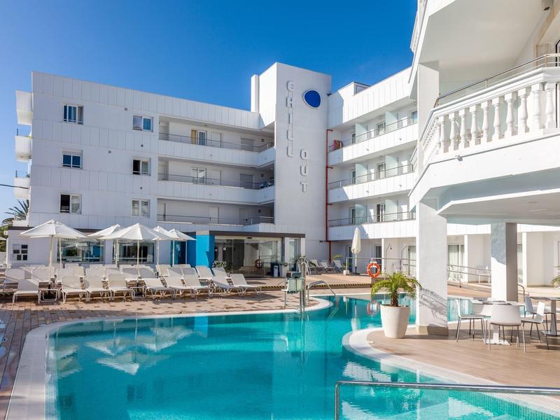 Complesso alberghiero moderno con piscina all'aperto, lettini e cielo blu sullo sfondo.