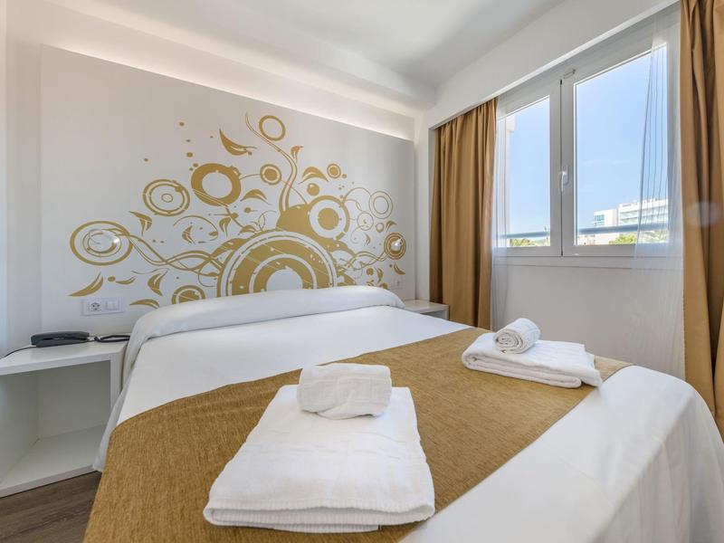 Camera d'hotel luminosa arredata con letto matrimoniale, decorazione murale e grandi finestre con tende.