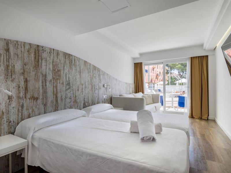 Camera d'hotel luminosa con due letti, parete in legno e balcone con vista sulla piscina.