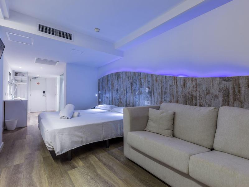 Camera d'hotel moderna con divano, letto grande, pavimento in legno e illuminazione indiretta.